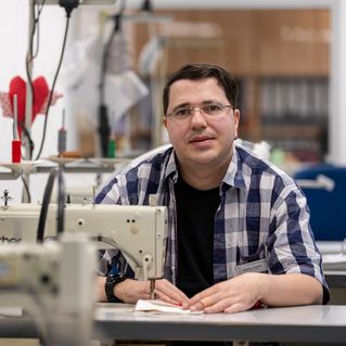 Matthias Schütze sitzt an der Nähmaschine und schaut in die Kamera